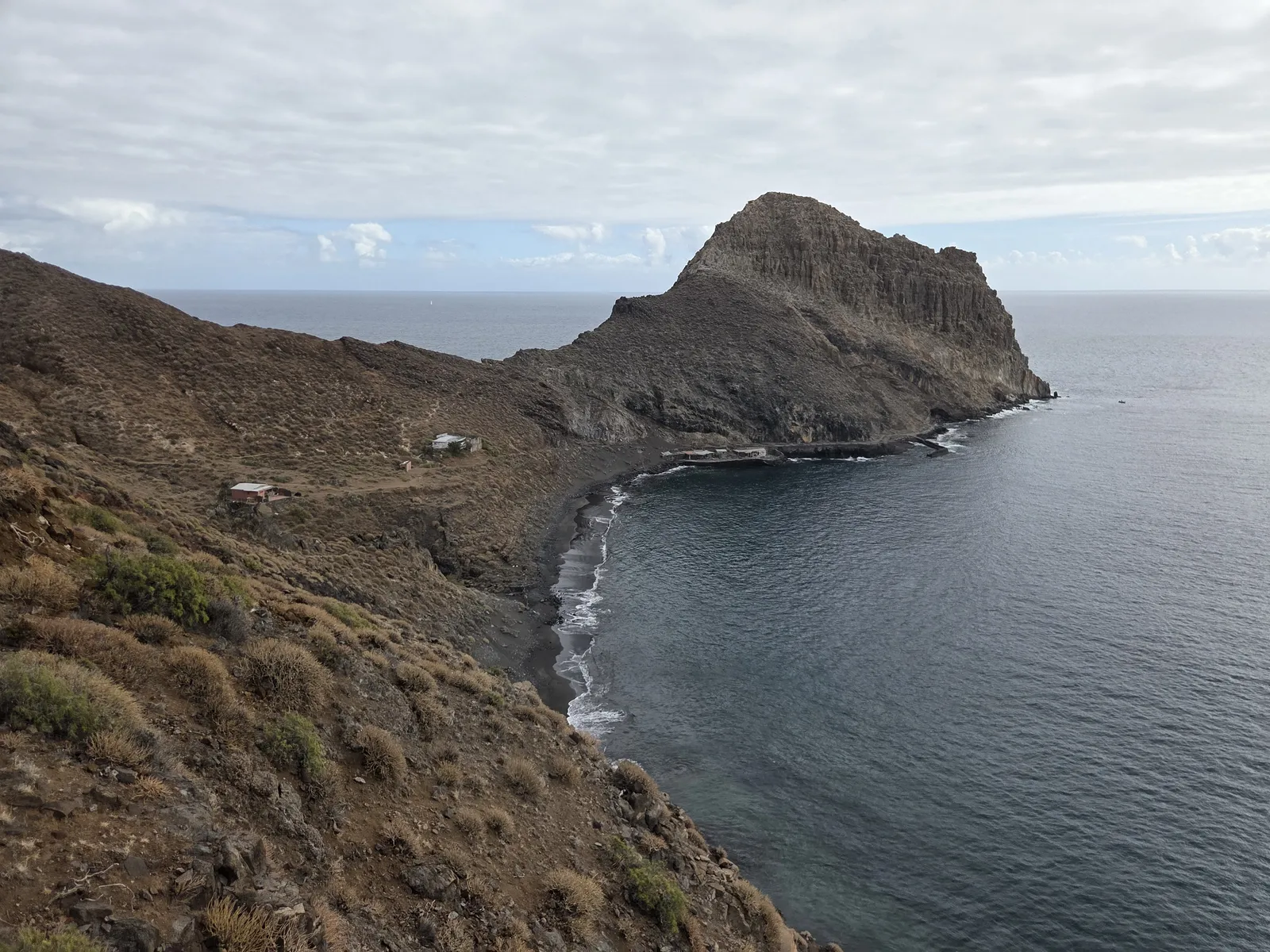 Antequera Beach curving beneath a rugged headland, viewed from the hillside