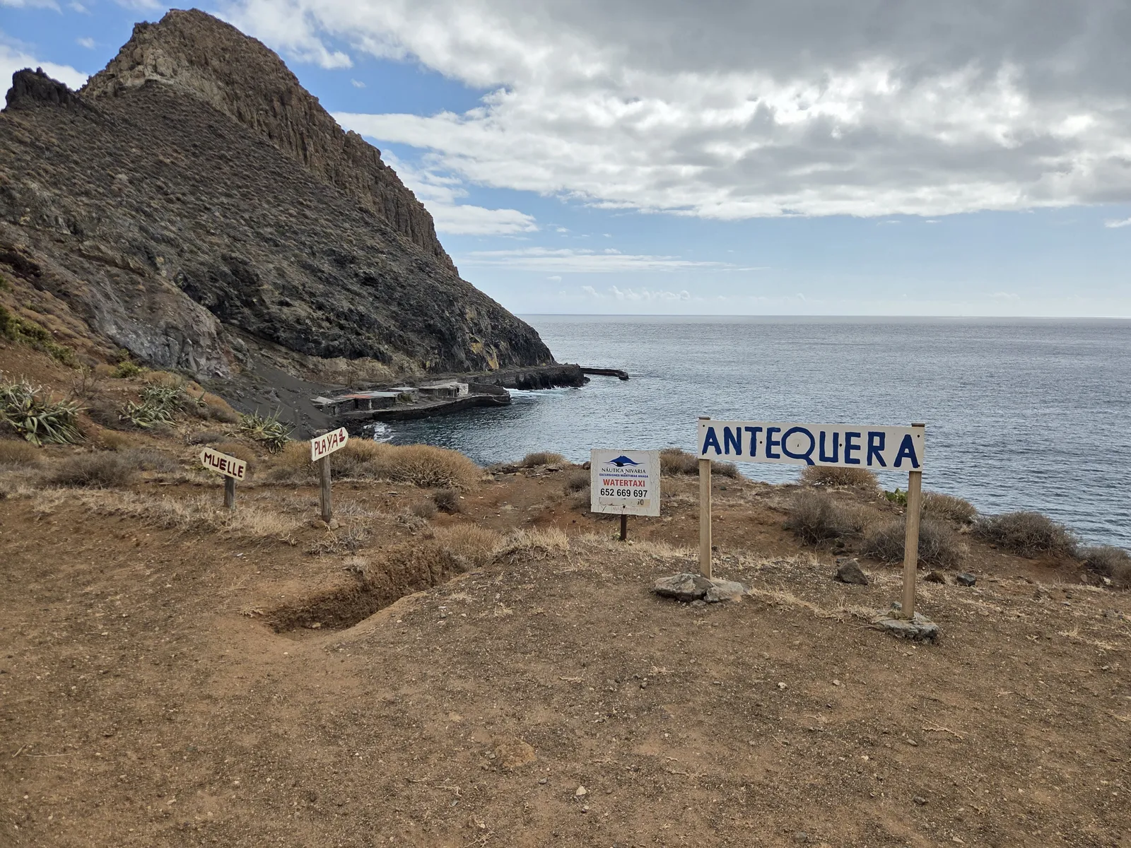 Antequera sign and wooden arrows pointing towards the beach and pier beneath the rocky headland