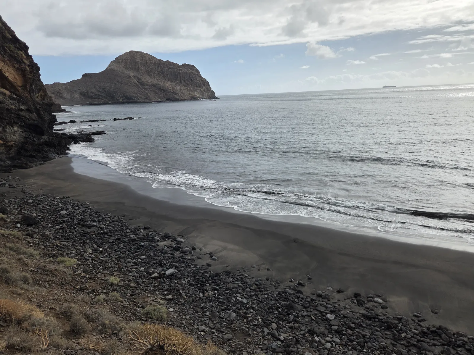 Dark sand and rounded stones at Playa de Zápata beneath volcanic coastal cliffs