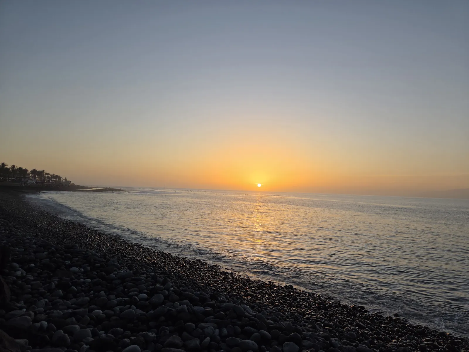 Sun setting over the Atlantic beside a dark pebble shoreline in Costa Adeje