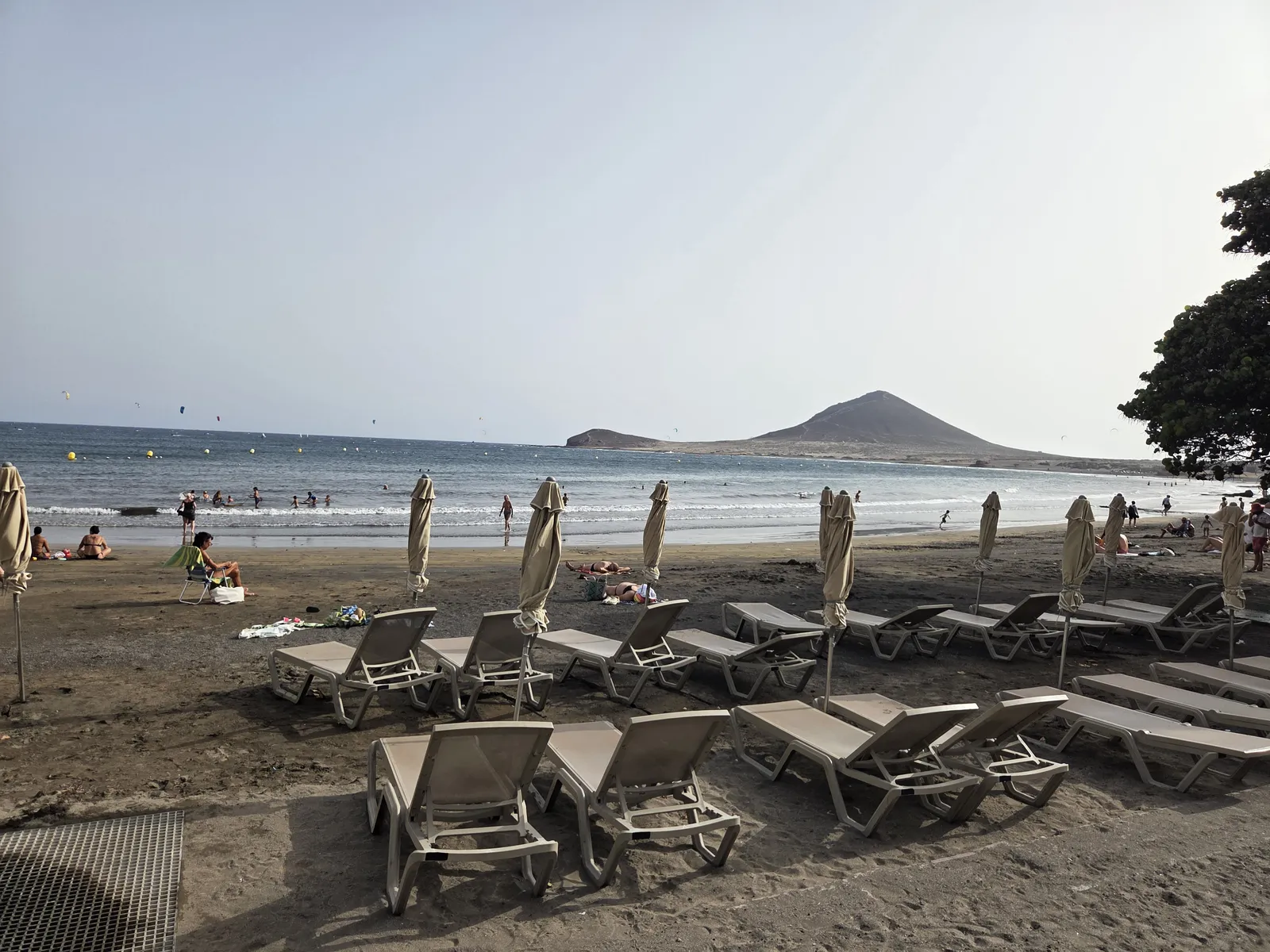 Sun loungers beside El Médano beach, with swimmers in the bay and Montaña Roja beyond