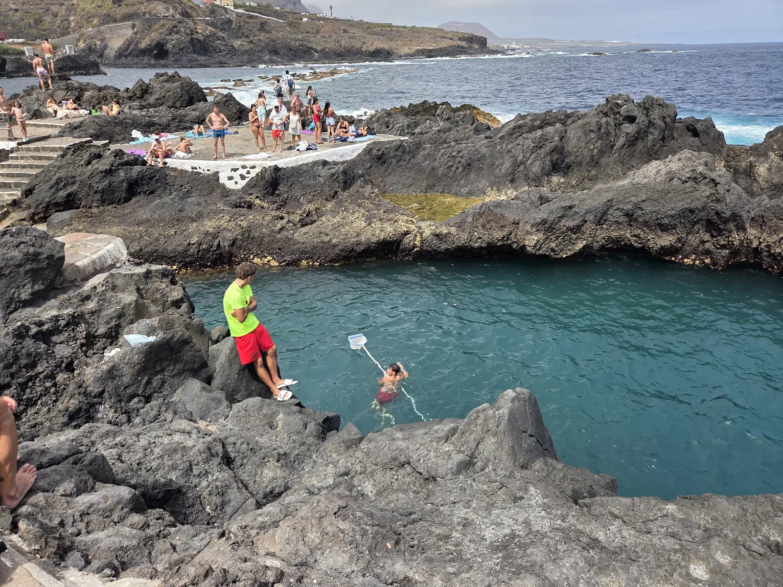 Swimmers in a turquoise seawater pool surrounded by uneven dark volcanic rock at El Caletón