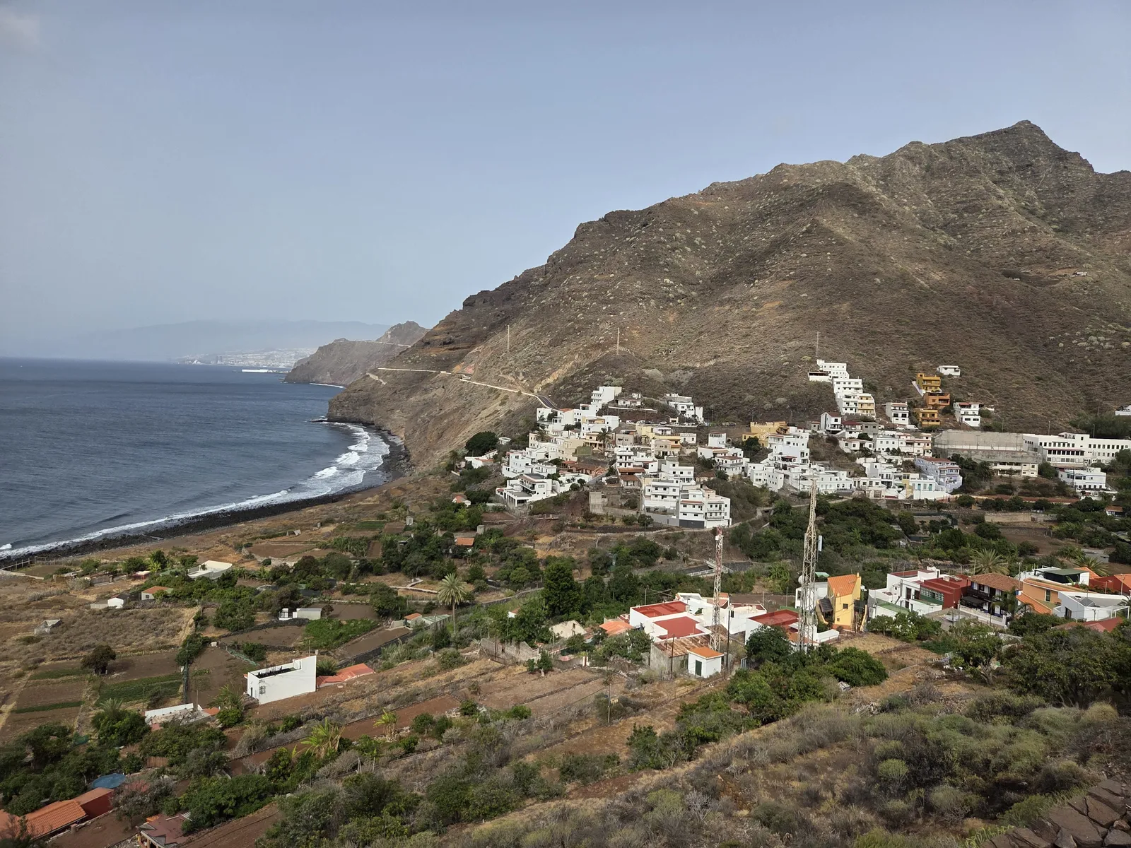 White houses and cultivated plots in Igueste de San Andrés beneath a rocky ridge beside the Atlantic