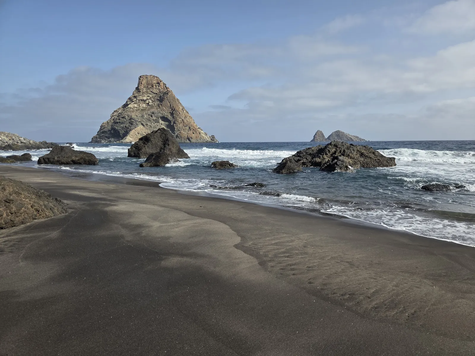 Black sand and shoreline boulders at Las Breñas Beach with the Roques de Anaga offshore