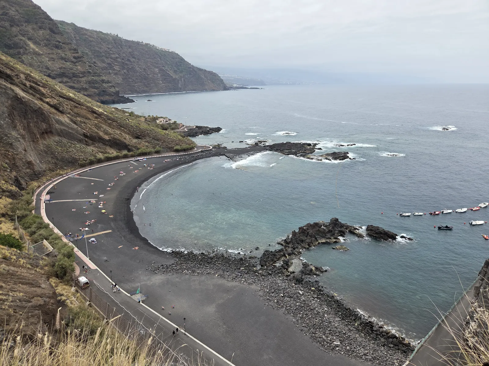 Curving black-sand Playa de la Arena beneath cliffs, with a promenade, offshore rocks and small boats
