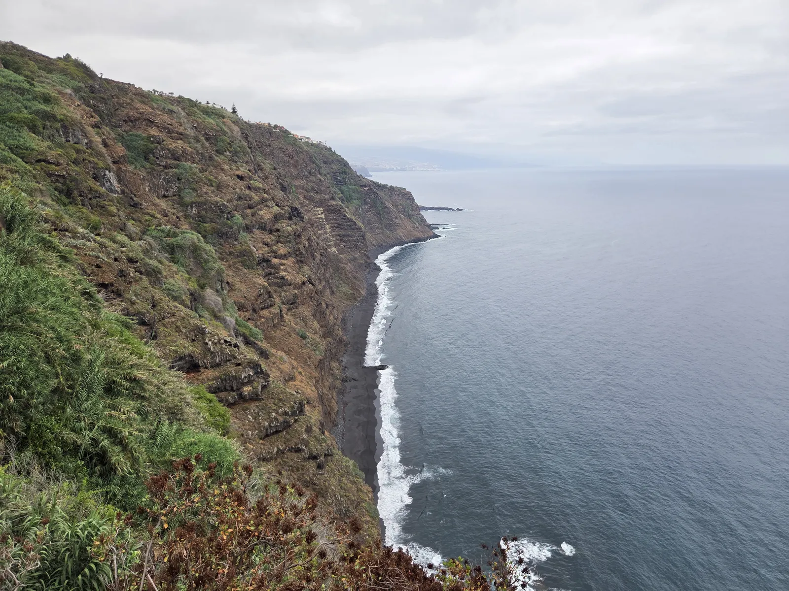 Steep volcanic cliffs above the dark shoreline of La Garañona, with waves breaking along the beach