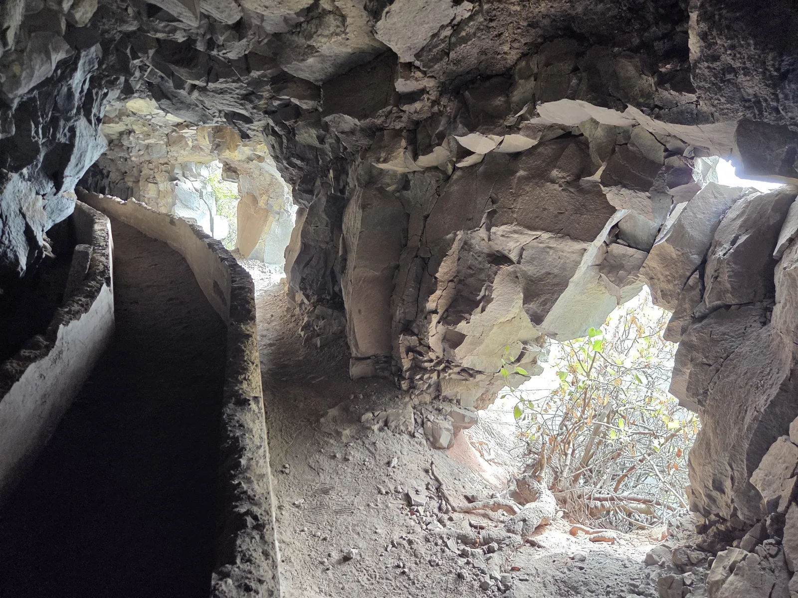 Rock-cut water channel curving through a tunnel beside openings in the mountainside