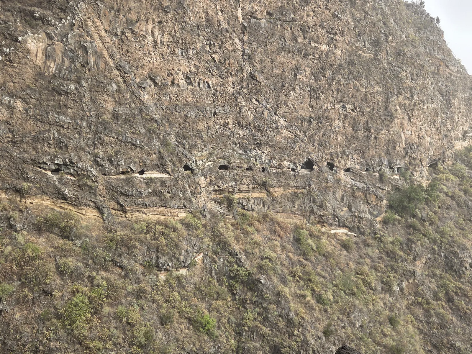 Small tunnel windows forming a horizontal line across a steep volcanic rock face