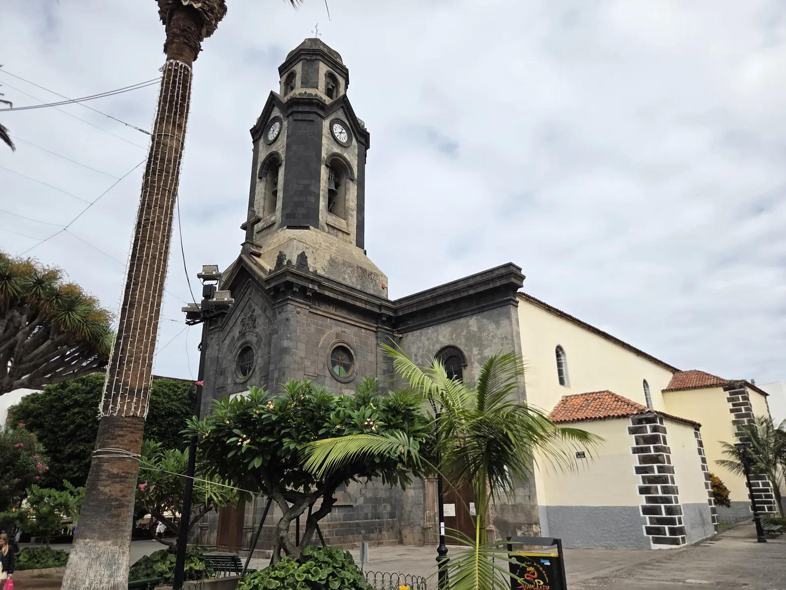 Stone clock tower and pale exterior of Nuestra Señora de la Peña de Francia church behind palms