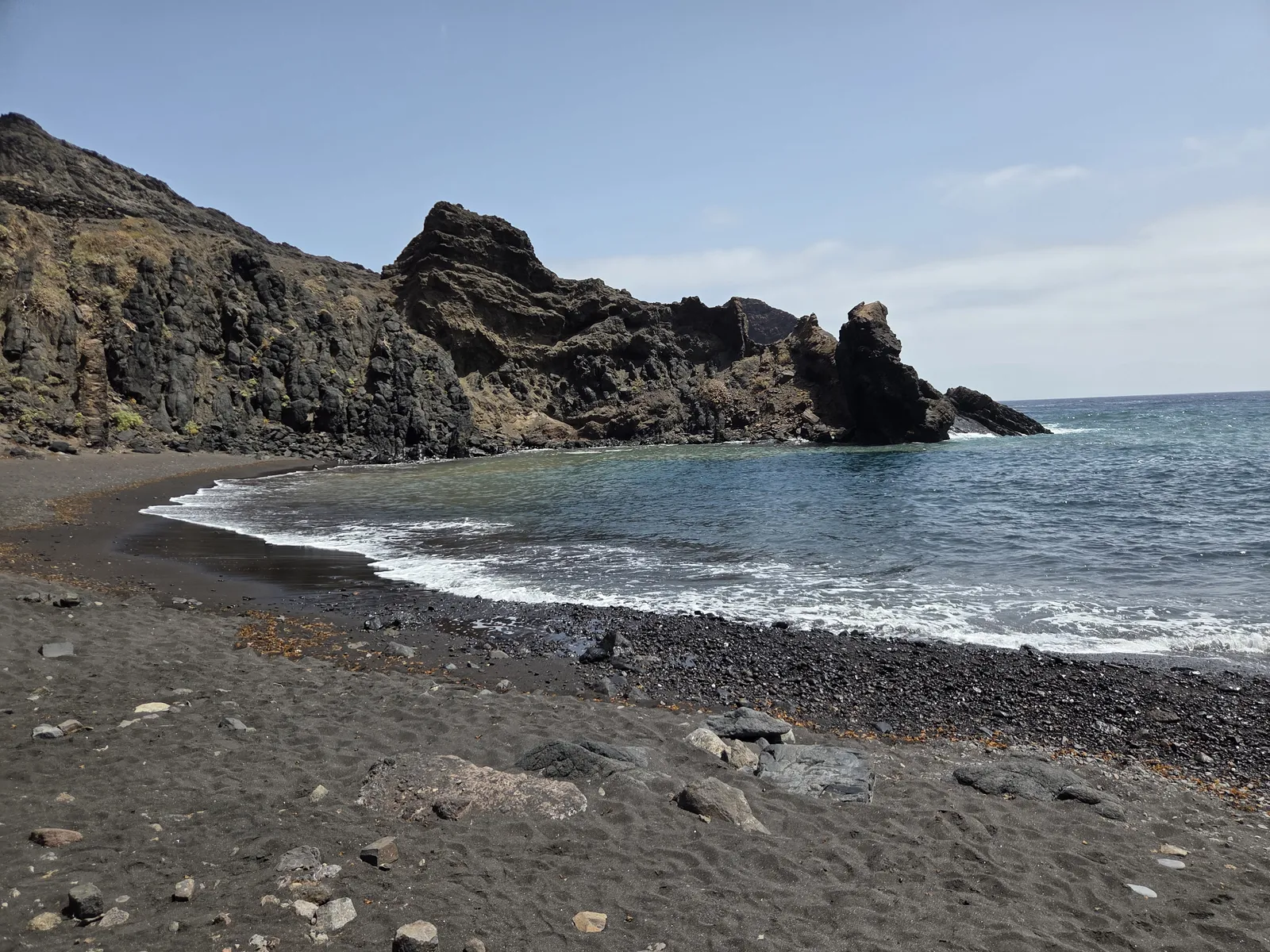 Dark sand and pebbles on Roque Bermejo Beach beneath jagged volcanic cliffs