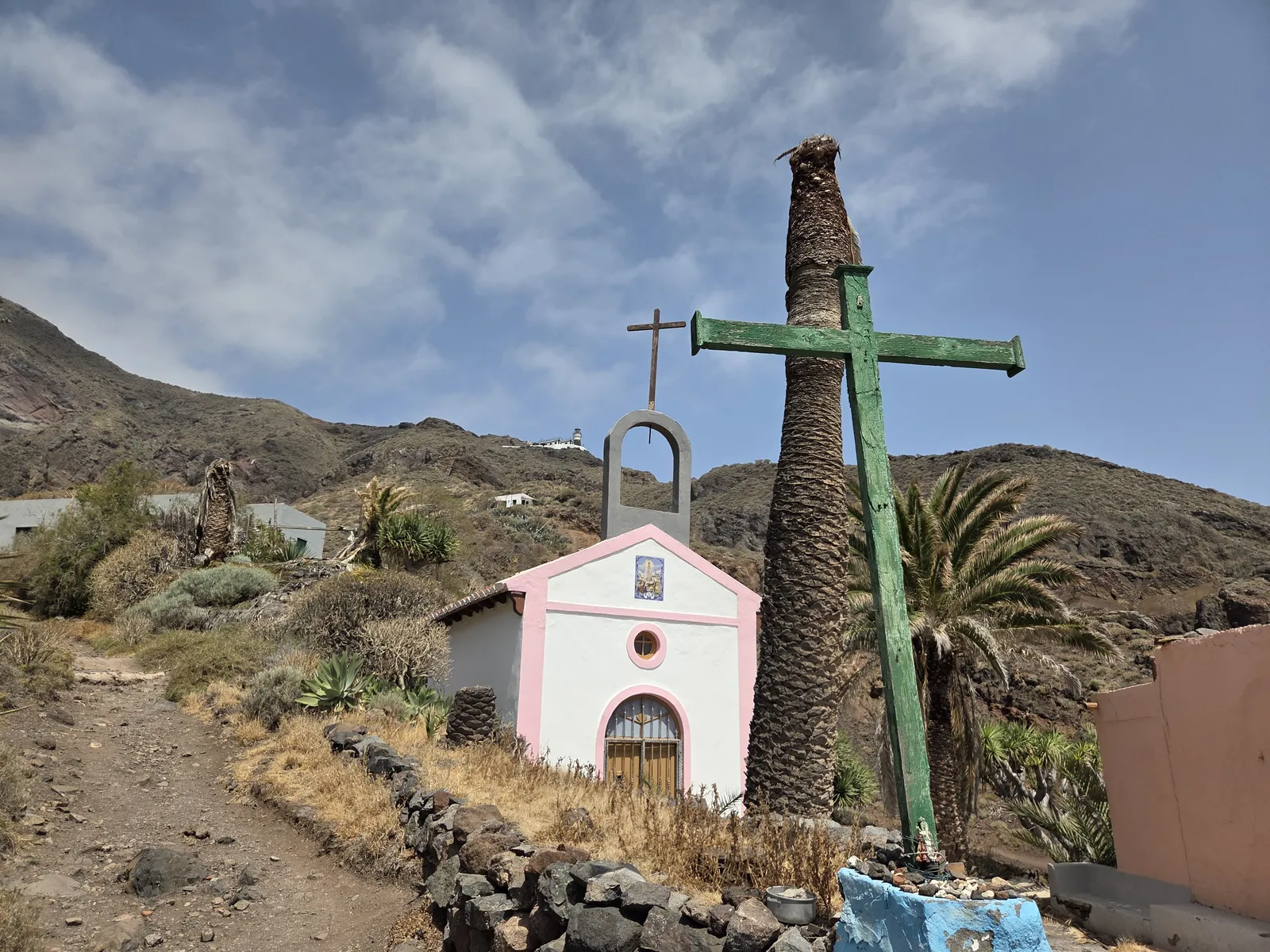 Small white chapel with pink trim beside a green wooden cross in Roque Bermejo