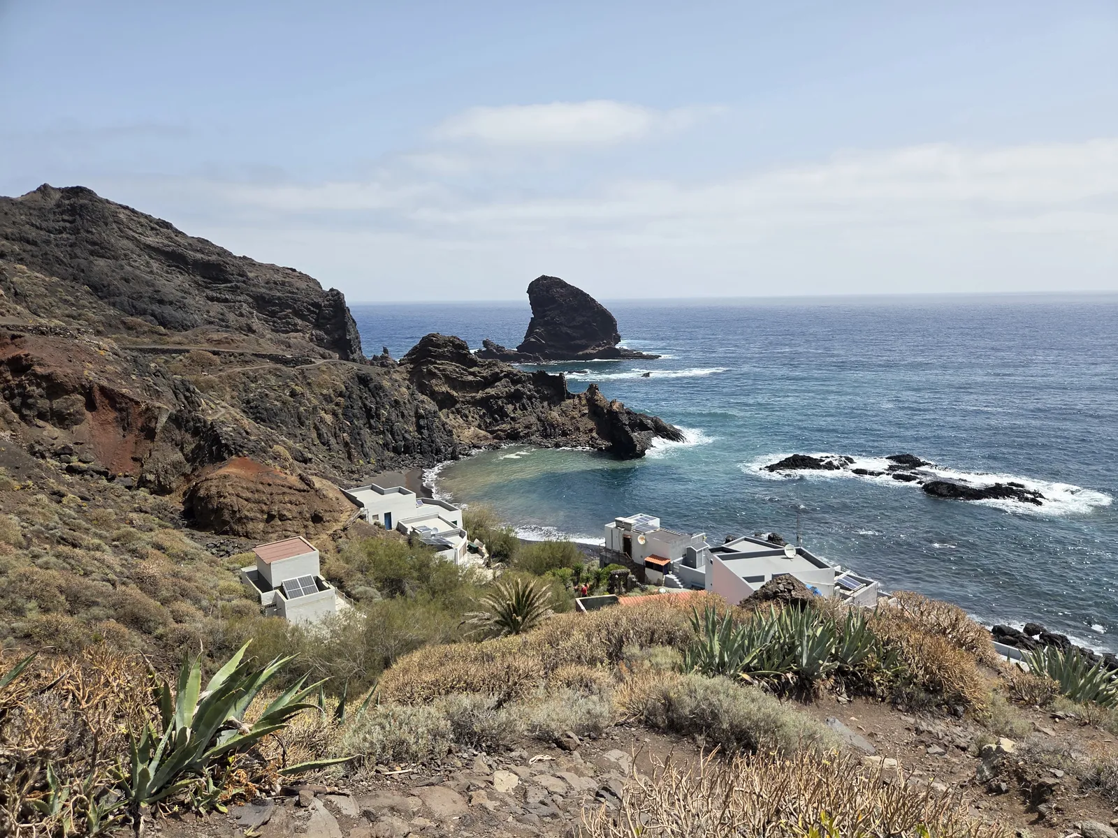 White houses above Roque Bermejo’s dark beach, with rugged coastal rocks and an offshore sea stack