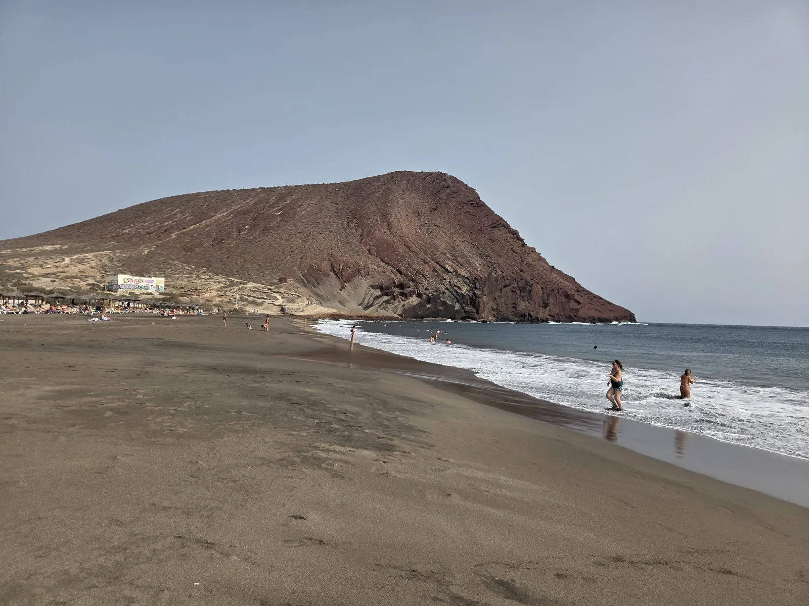 Montaña Roja rising above La Tejita Beach, with walkers beside the breaking waves