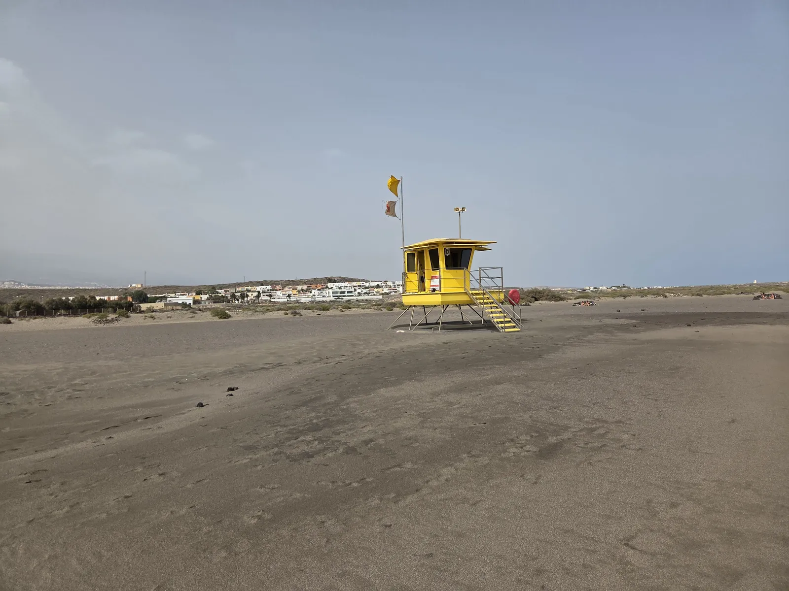 Yellow lifeguard tower and beach flags on the broad sand at La Tejita