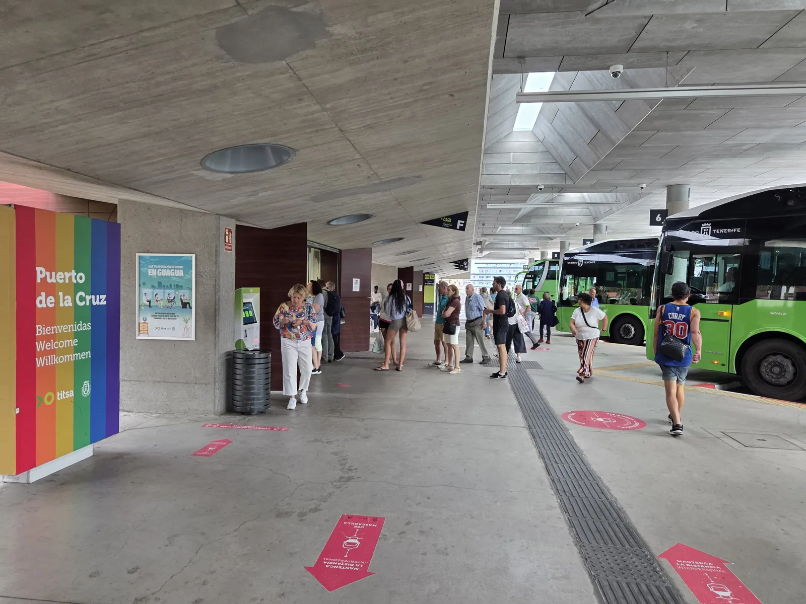 Passengers beside green TITSA buses at the covered Puerto de la Cruz bus station